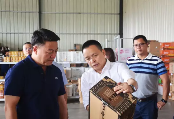盐津铺子董事长张学武(左二)向邱明宏(左一)介绍电商产品外包装箱